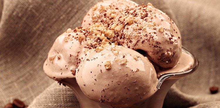 Four scoops of chocolate or coffee ice cream sprinkled with nuts and ground chocolate in a parfait glass on a burlap cloth with some coffee beans on it