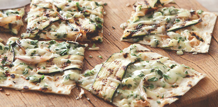 Squares of grilled pizza with herbs, cheese, and sliced zucchini on top