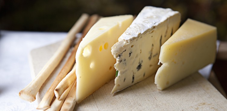 Three types of stinky French cheeses stand in a row next to thin breadsticks