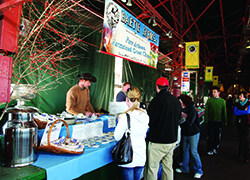 A man and woman behind a stand sell cheese.