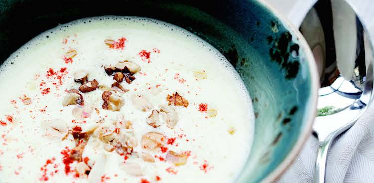 White cheese soup speckled with paprika and chopped hazelnuts in a blue pottery bowl