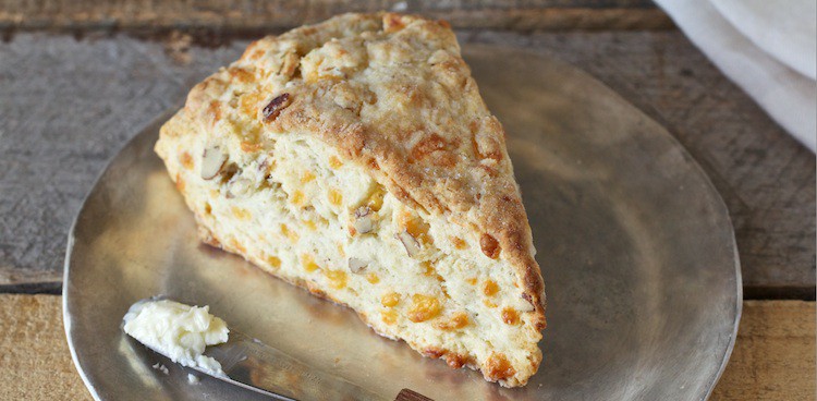 Baked scone dotted with cheddar cheese on a metallic plate with a butter knife