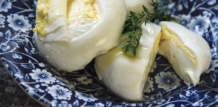 Two burrata filled with homemade butter on a blue patterned plate with a fresh thyme garnish