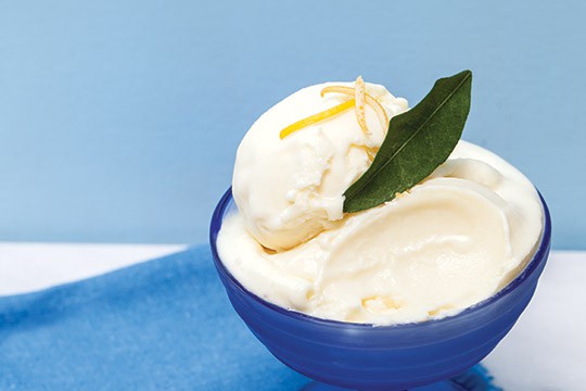 Lemon mascarpone ice cream in a bowl topped with lemon zest and garnished with a bay leaf