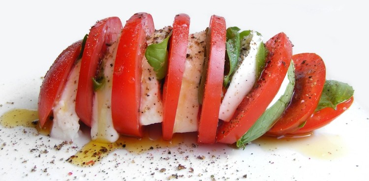 Slices of juicy tomato, creamy mozzarella, and fresh basil layered together and drizzled with olive oil and cracked black pepper