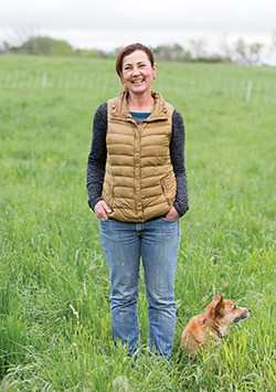 Dutch Girl Creamery's Charuth Van Beuzekom standing in the pasture with her Welsh corgi, Penny.