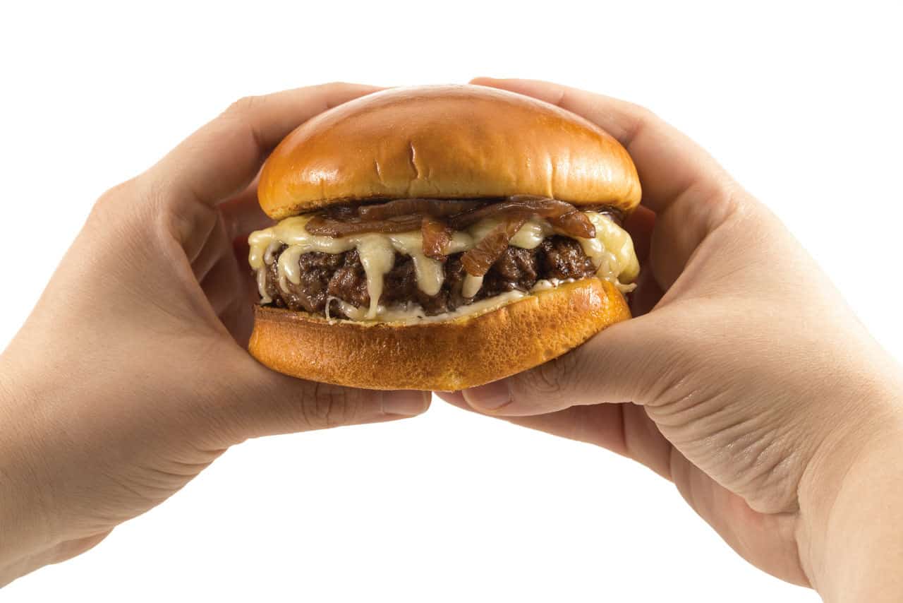 hands holding a burger topped with gruyere and caramelized onions