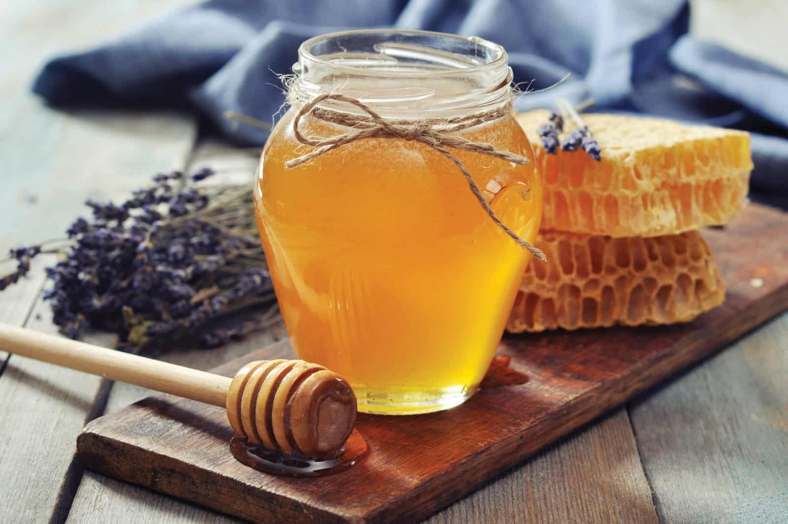Honey in jar with honey dipper on vintage wooden background.
